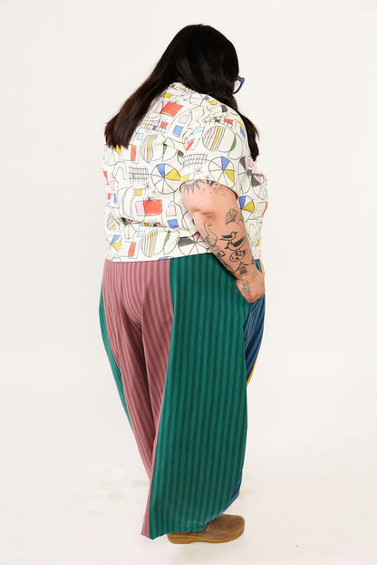 Person wearing a colorful patterned top and long pants on a white background