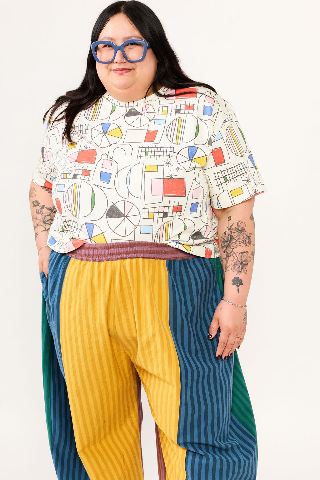 Person wearing a colorful geometric-patterned shirt and multicolored pants on a white background