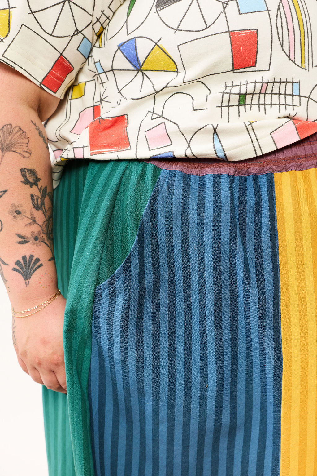 Person wearing a colorful geometric-patterned top with a striped pants from Lilla Barn Clothing