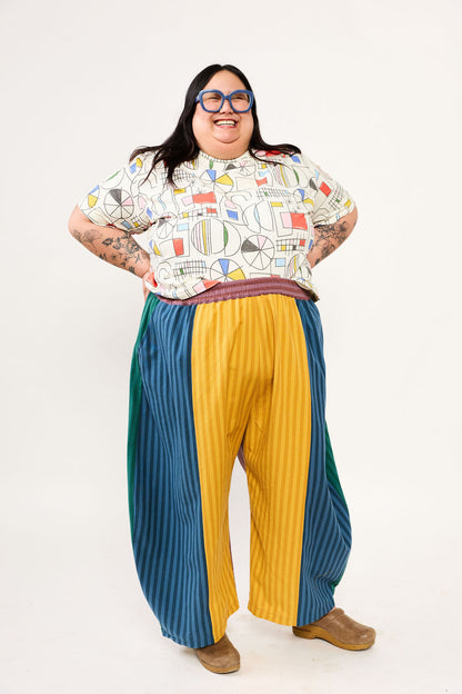 Person wearing a patterned shirt and colorful pants on a white background