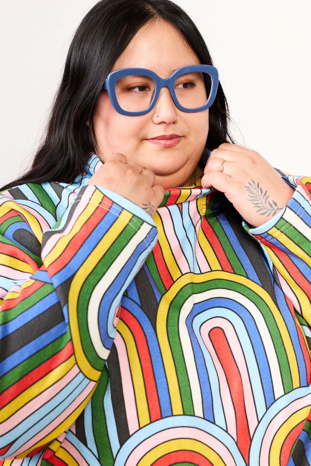 Person wearing a colorful, patterned outfit with blue glasses against a plain background