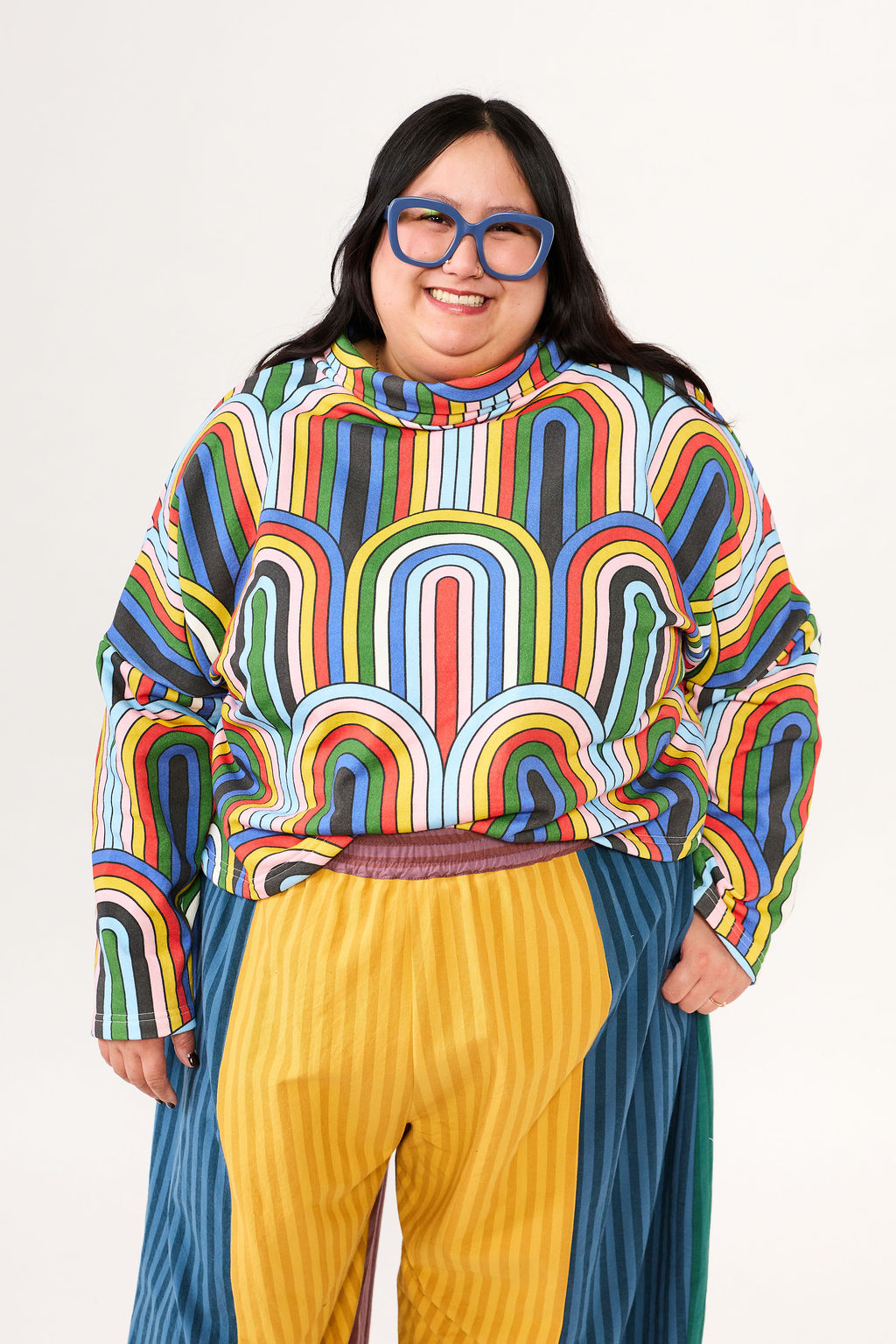 Person wearing a colorful striped sweater and yellow pants on a white background
