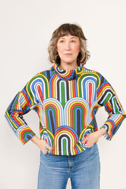 Owner of Lilla Barn Clothing wearing a colorful, rainbow pattern shirt with a plain background