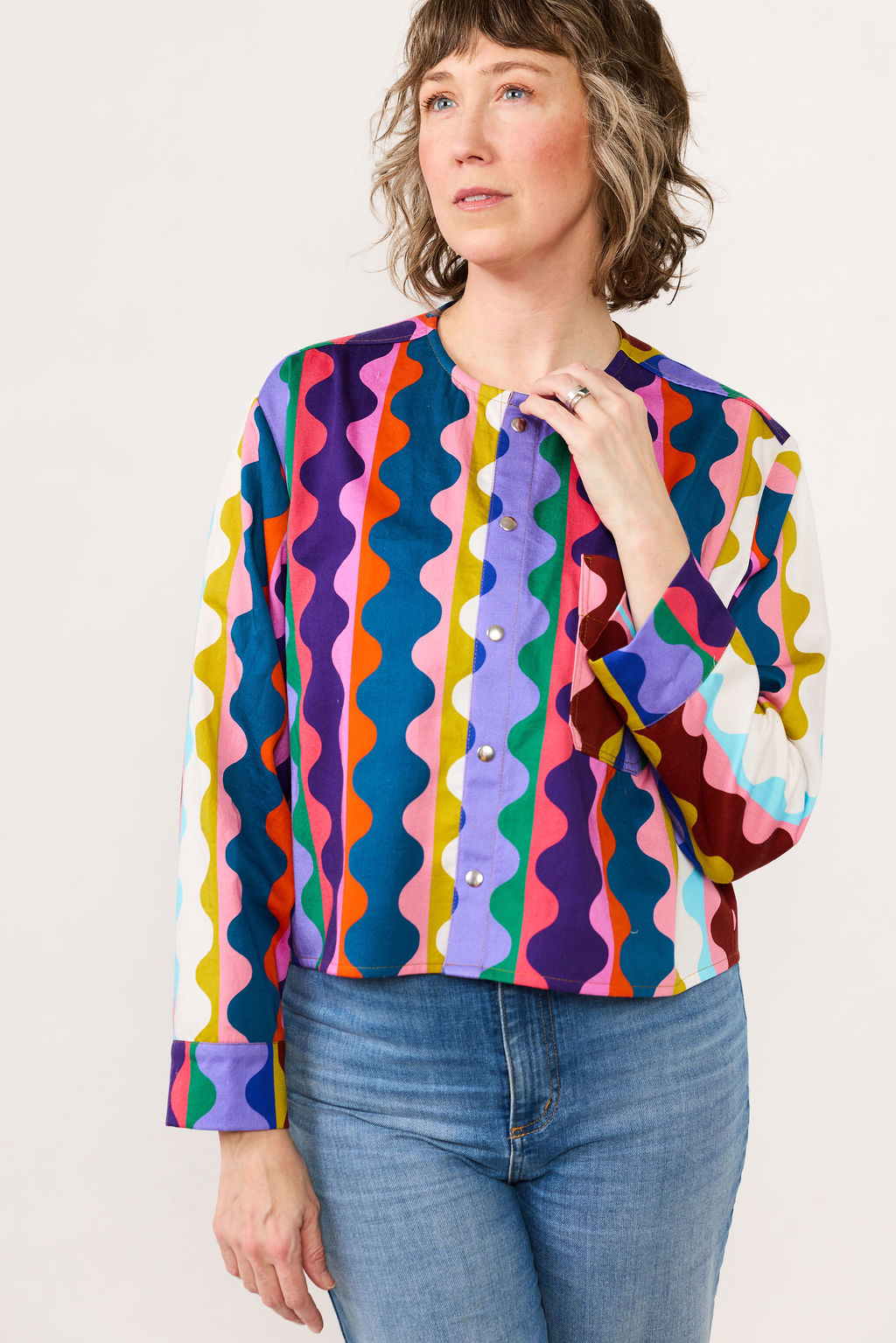 Lilla Barn owner wearing a colorful patterned blouse and blue jeans on a white background