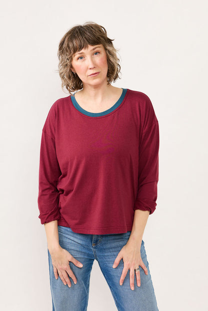Woman wearing a maroon long-sleeve shirt and blue jeans against a white background