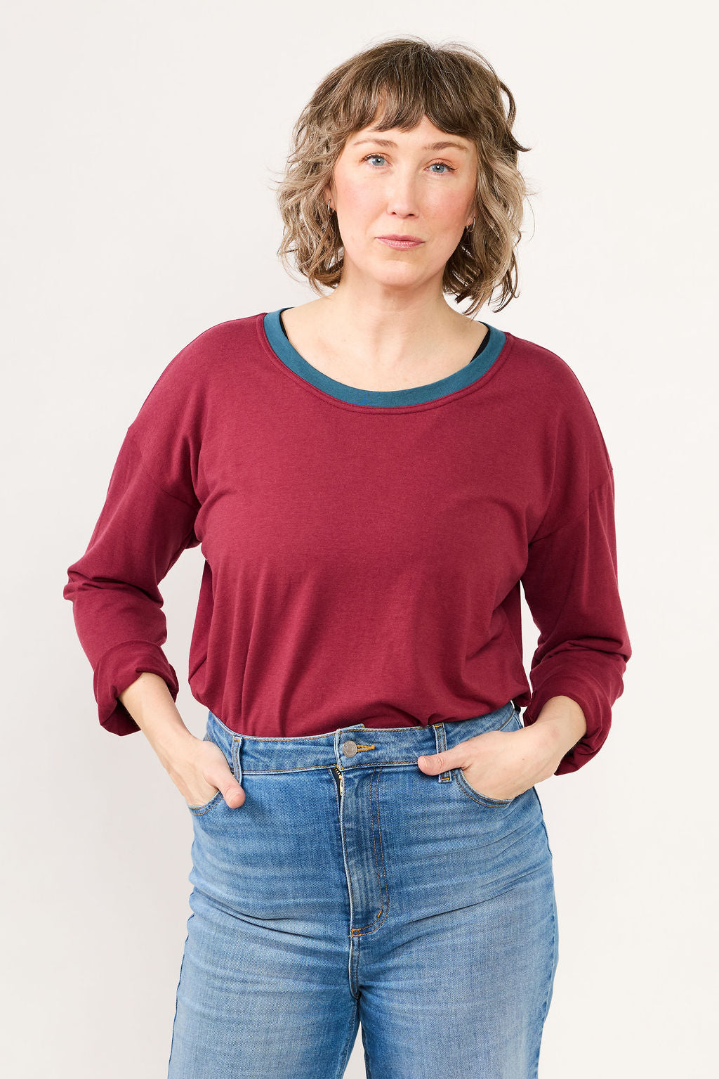 Woman wearing a maroon top and blue jeans against a white background