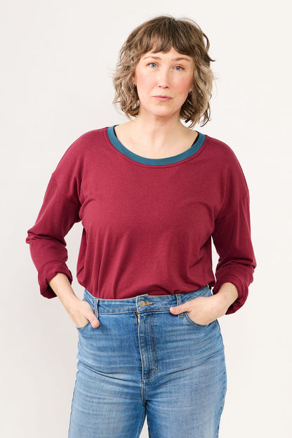 Woman wearing a maroon top and blue jeans against a white background