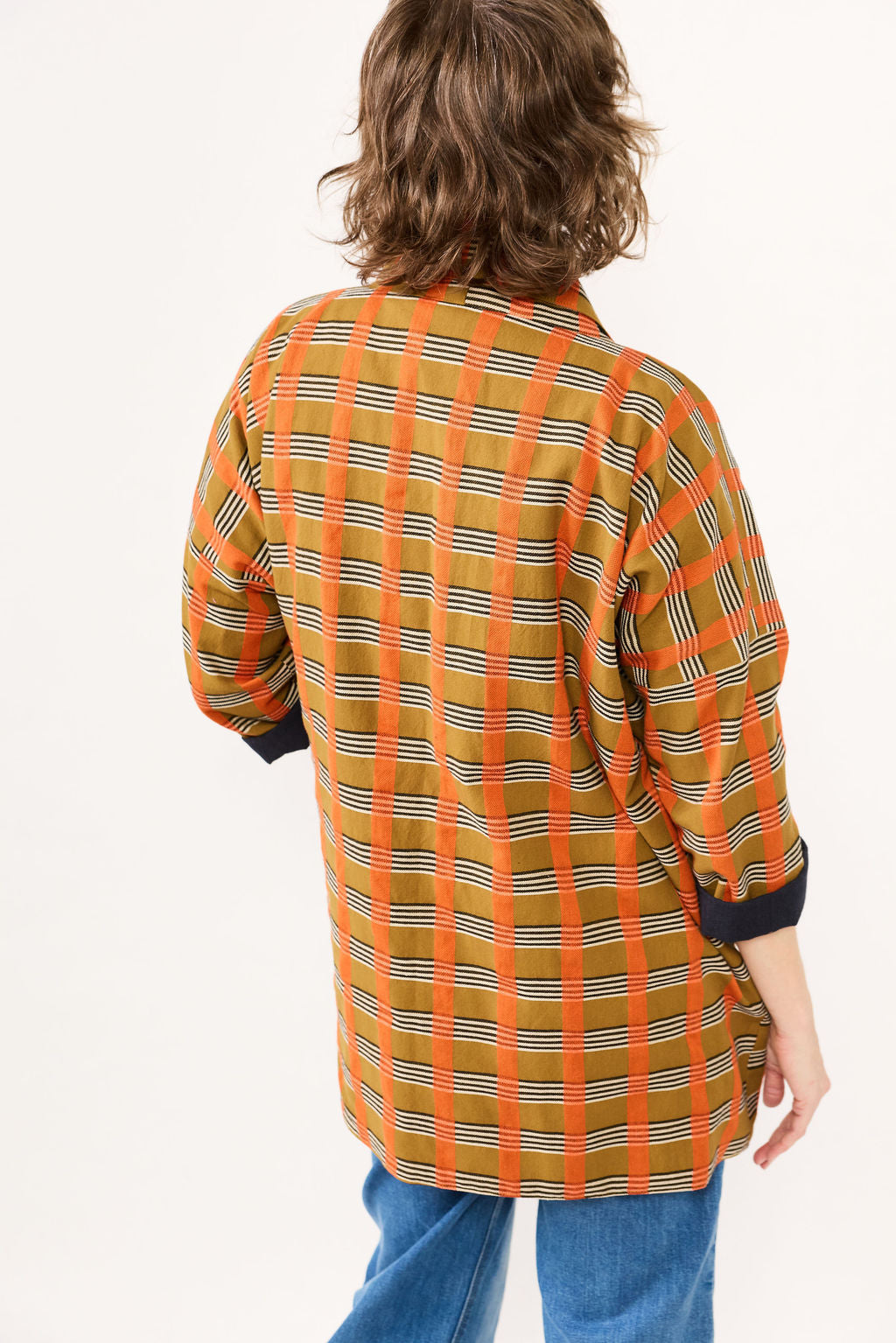 Person wearing a plaid shirt with orange and green pattern on a white background