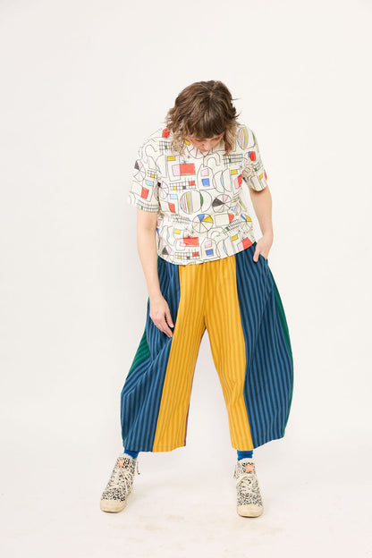 Person wearing a colorful outfit with a patterned shirt and pleated pants on a white background