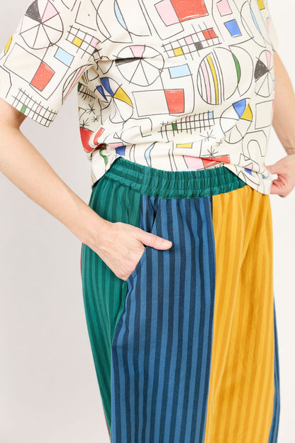 Person wearing a colorful geometric-patterned shirt and multicolored striped pants on a plain background