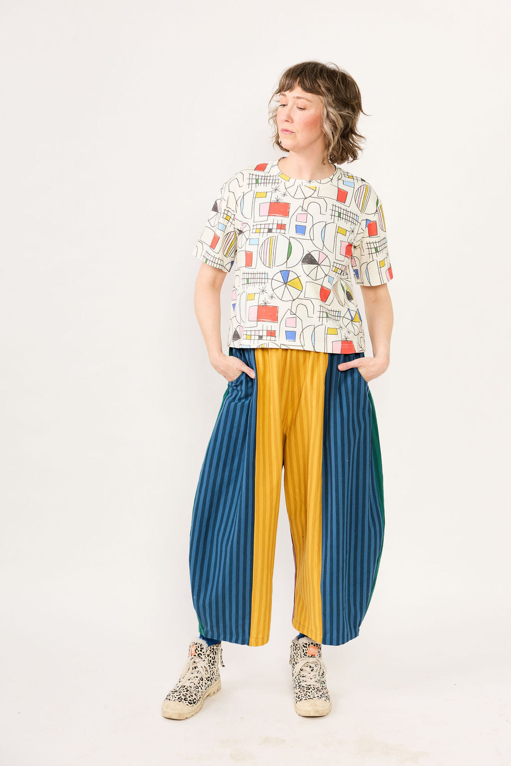 Person wearing a colorful patterned shirt and blue and yellow pants on a white background