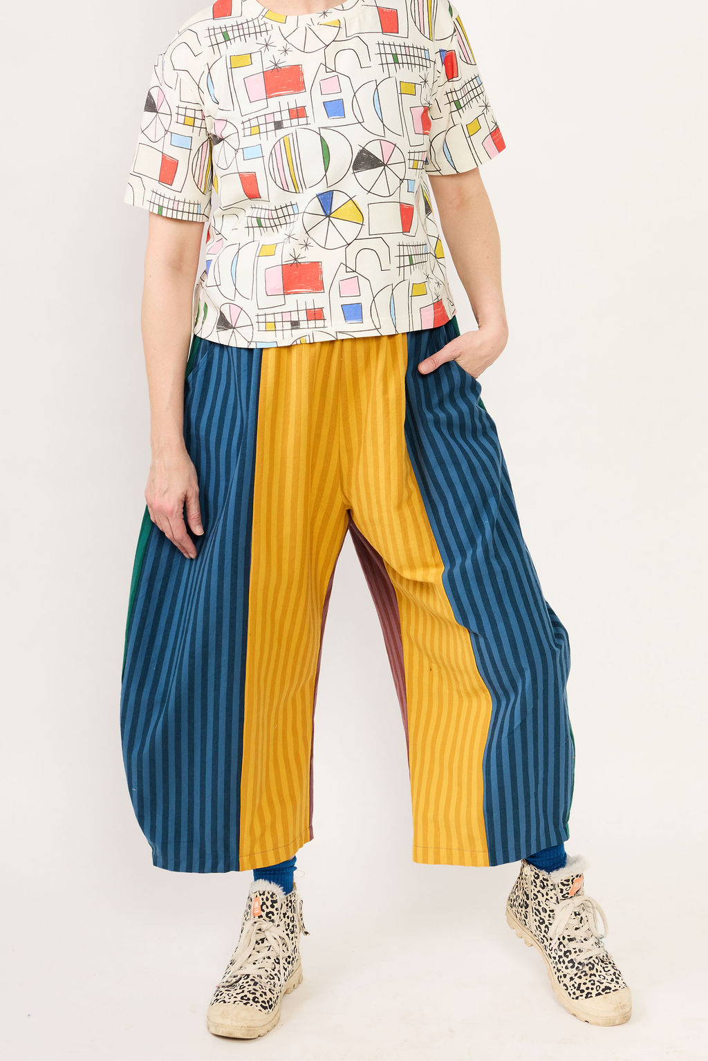Person wearing a colorful patterned shirt and blue and yellow striped pants on a white background