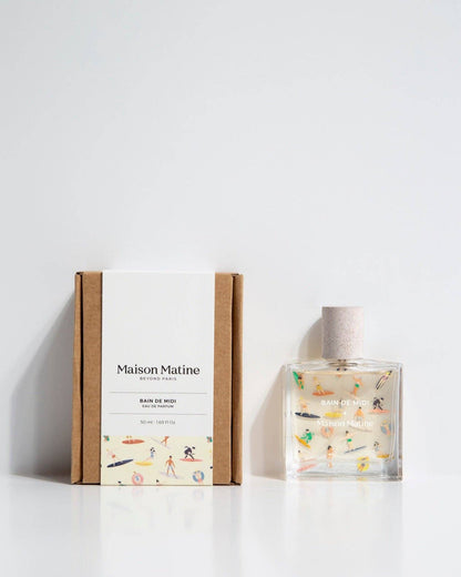 Glass bottle of Maison Matine edp next to the box packaging. Both have colorful art.
