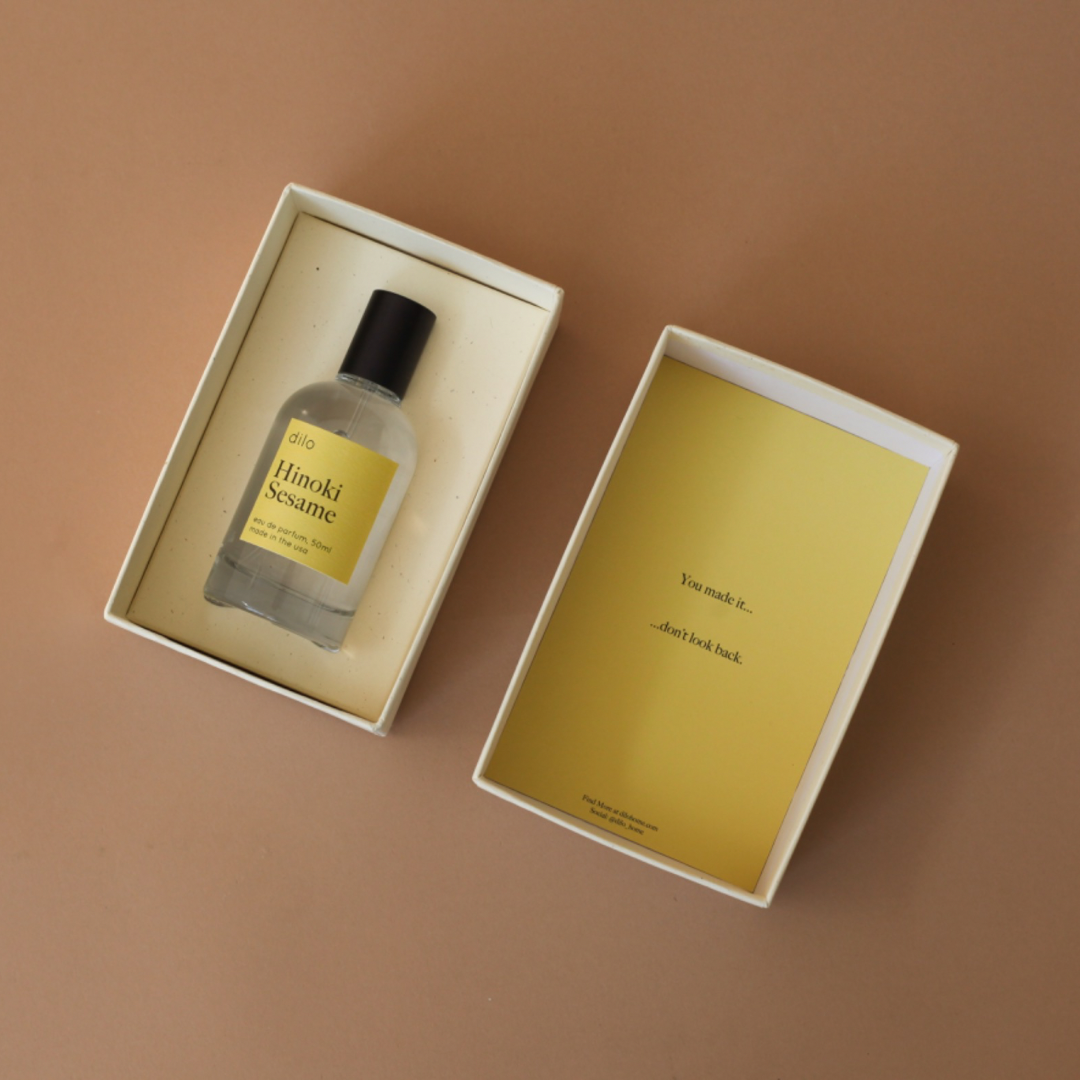 A clear glass bottle of Hinoki Sesame eau de parfum with a matte black sprayer on a neutral background 