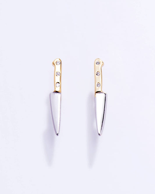 Pair of knife-shaped earrings with gold tops and silver blades on a light purple background