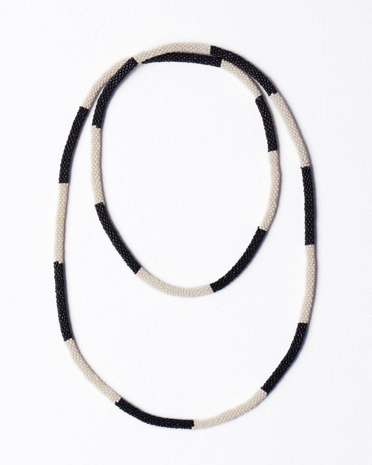 A beaded necklace with alternating black and cream-white textured beads, arranged in a loose loop on a plain white background.