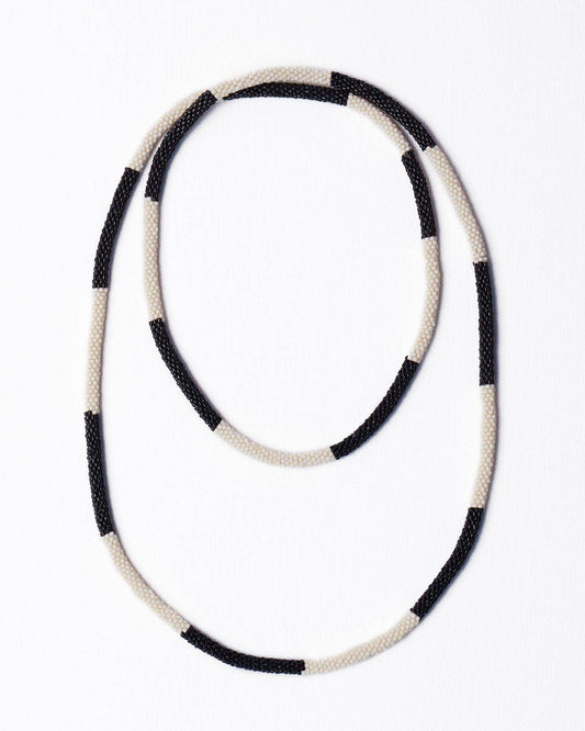 A beaded necklace with alternating black and cream-white textured beads, arranged in a loose loop on a plain white background.