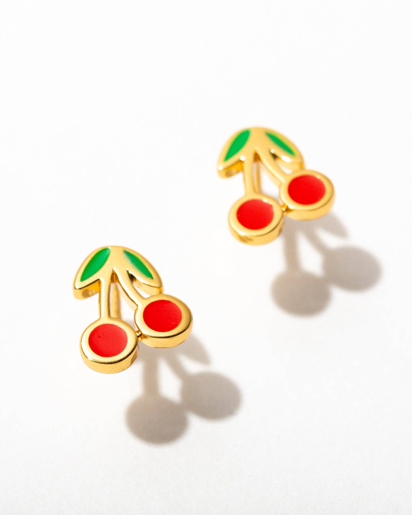 Gold cherry-shaped earrings with red stones on a white background