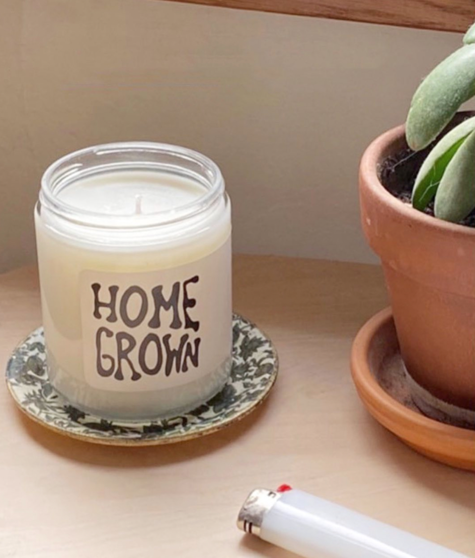 Candle with 'Home Grown' text on a coaster next to a potted plant and lighter.