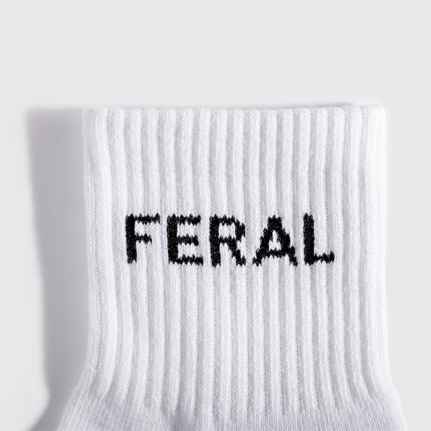 A close-up of a white ribbed knit sock with the word 'FERAL' knitted in black across the cuff, shown against a light gray background.