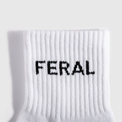 A close-up of a white ribbed knit sock with the word 'FERAL' knitted in black across the cuff, shown against a light gray background.