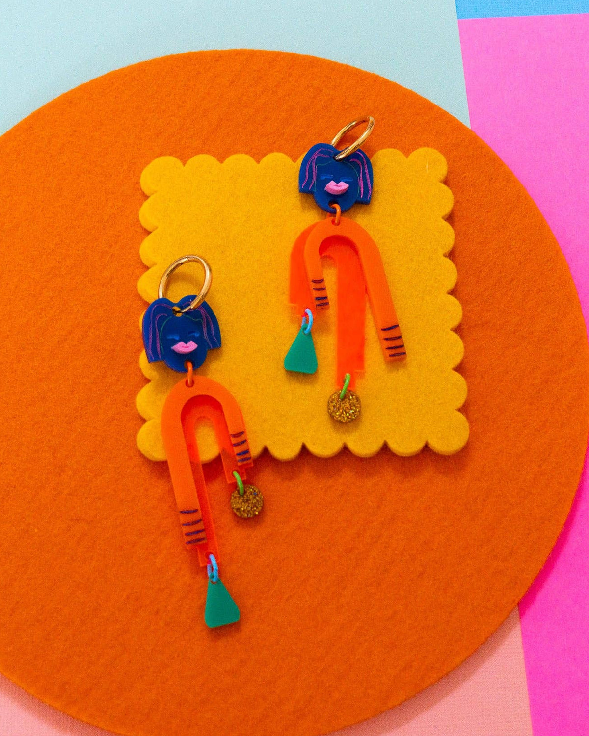 colorful dangly earrings made of acrylic and gold-plated stainless steel on a colorful background.
