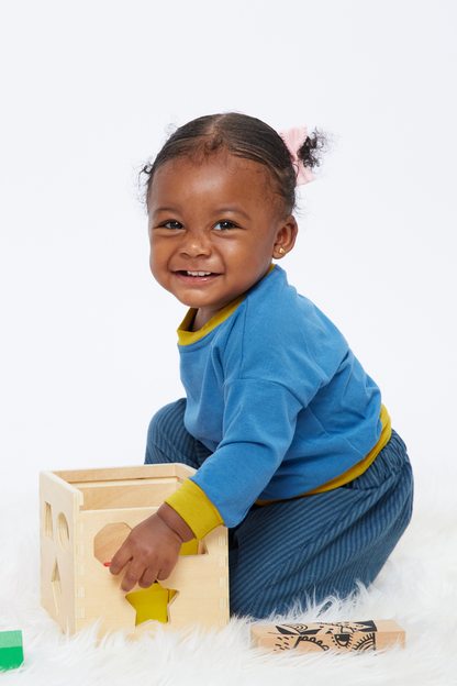 smiling baby playing with blocks wearing a gender-neutral blue and yellow pullover top