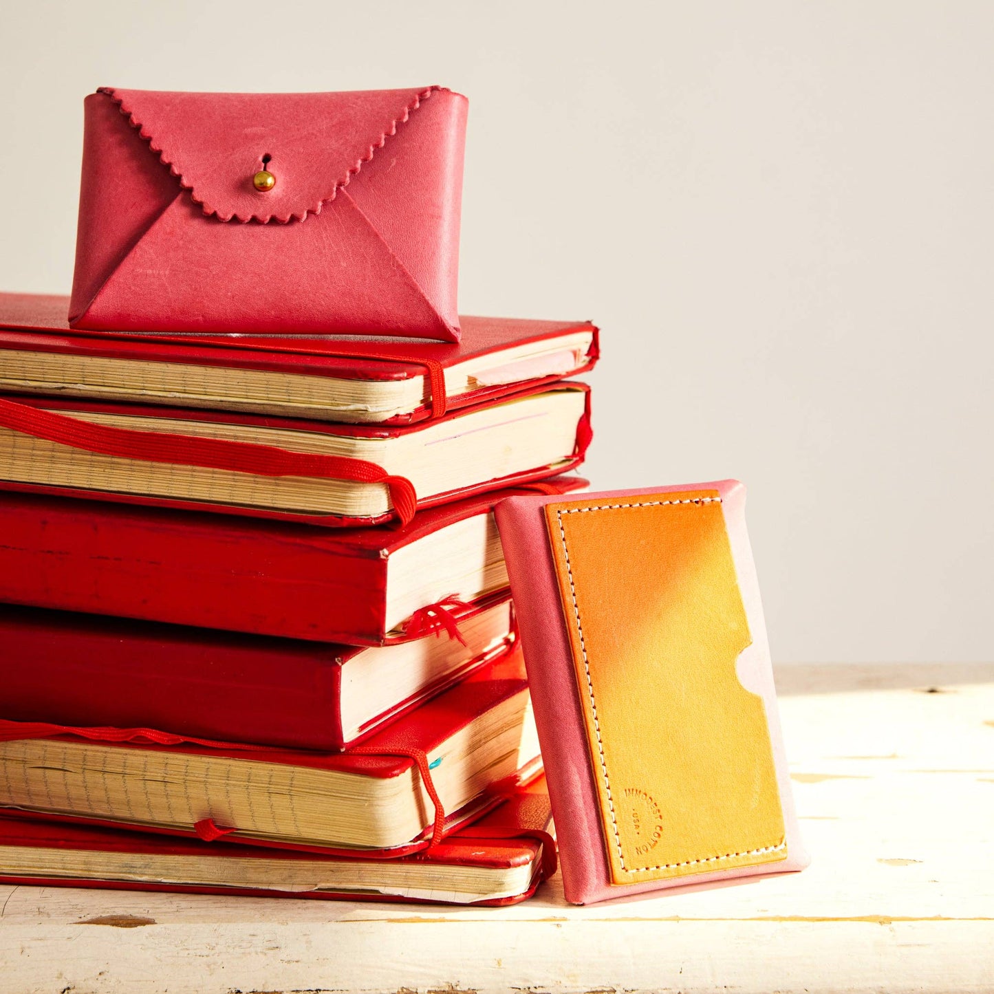 Stack of red books with a pink and orange leather wallet leaning on it. 