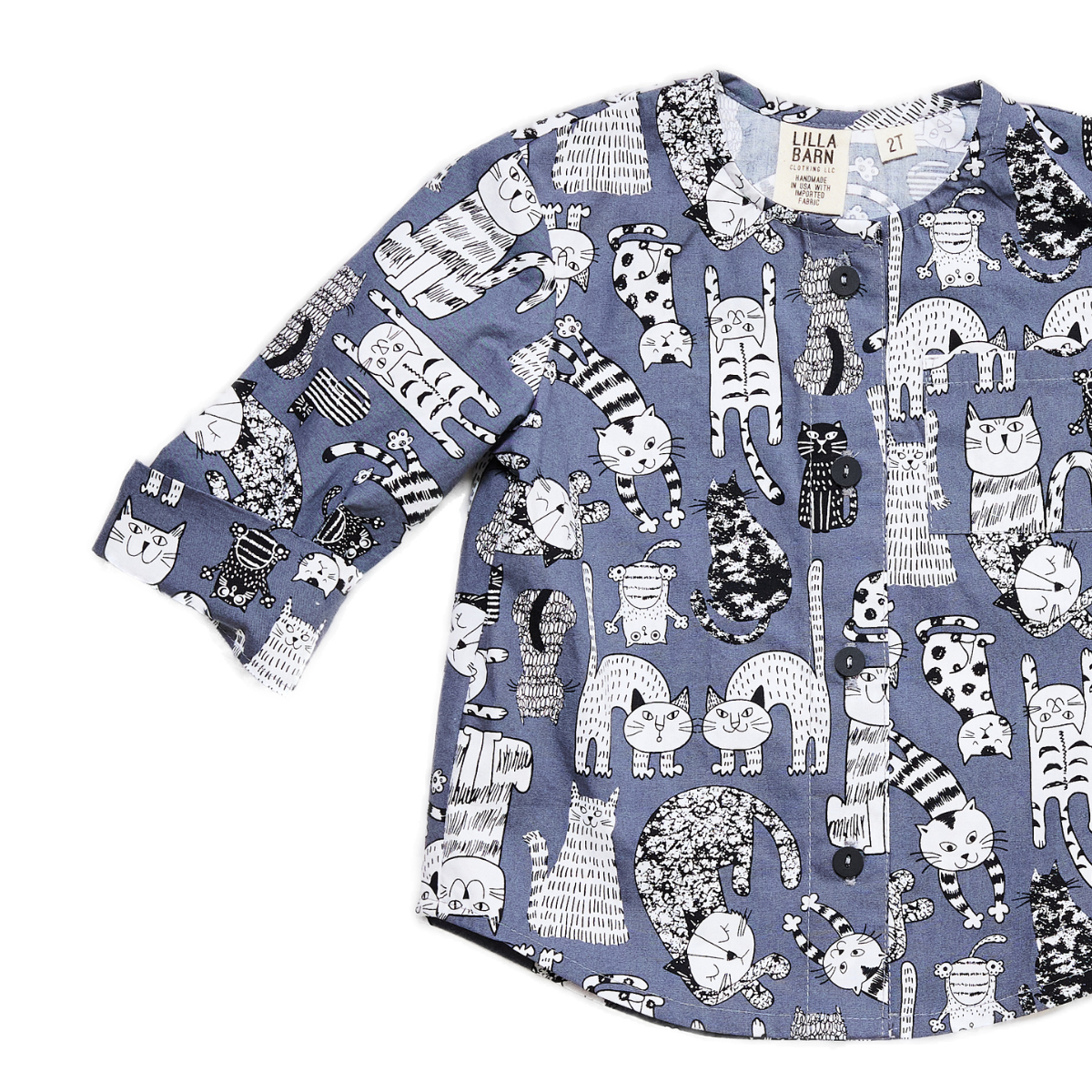 Toddler collar-less button down shirt with a chest pocket and sleeve cuffs that can be rolled up. The shirt is gray with illustrated black and white cats on it. 