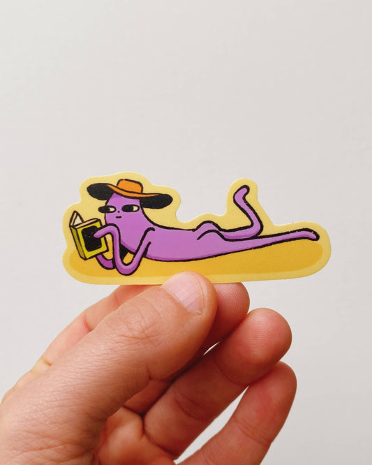 Hand holding a colorful sticker of a person lounging with a hat on a plain background