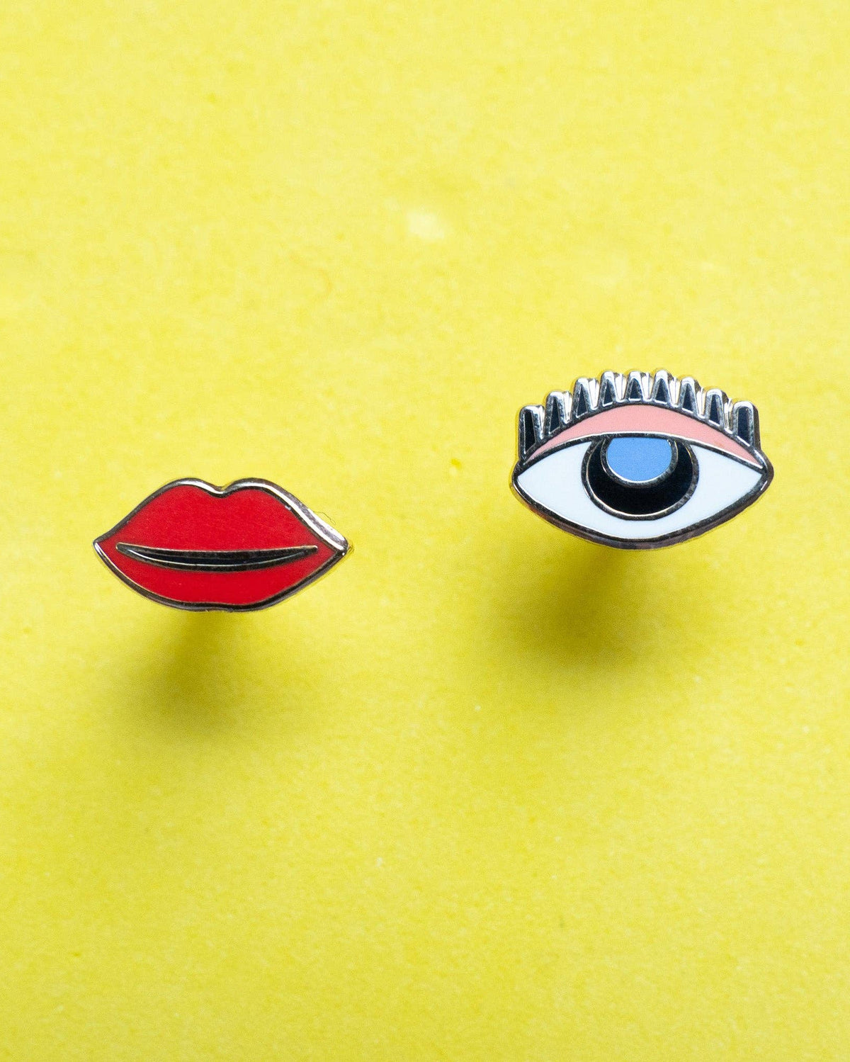 Mismatch stud earrings with one eye and one set of lips. sterling silver posts on a yellow background