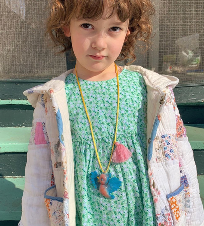 Child wearing a green dress with a floral-patterned jacket and a necklace with a fish pendant.