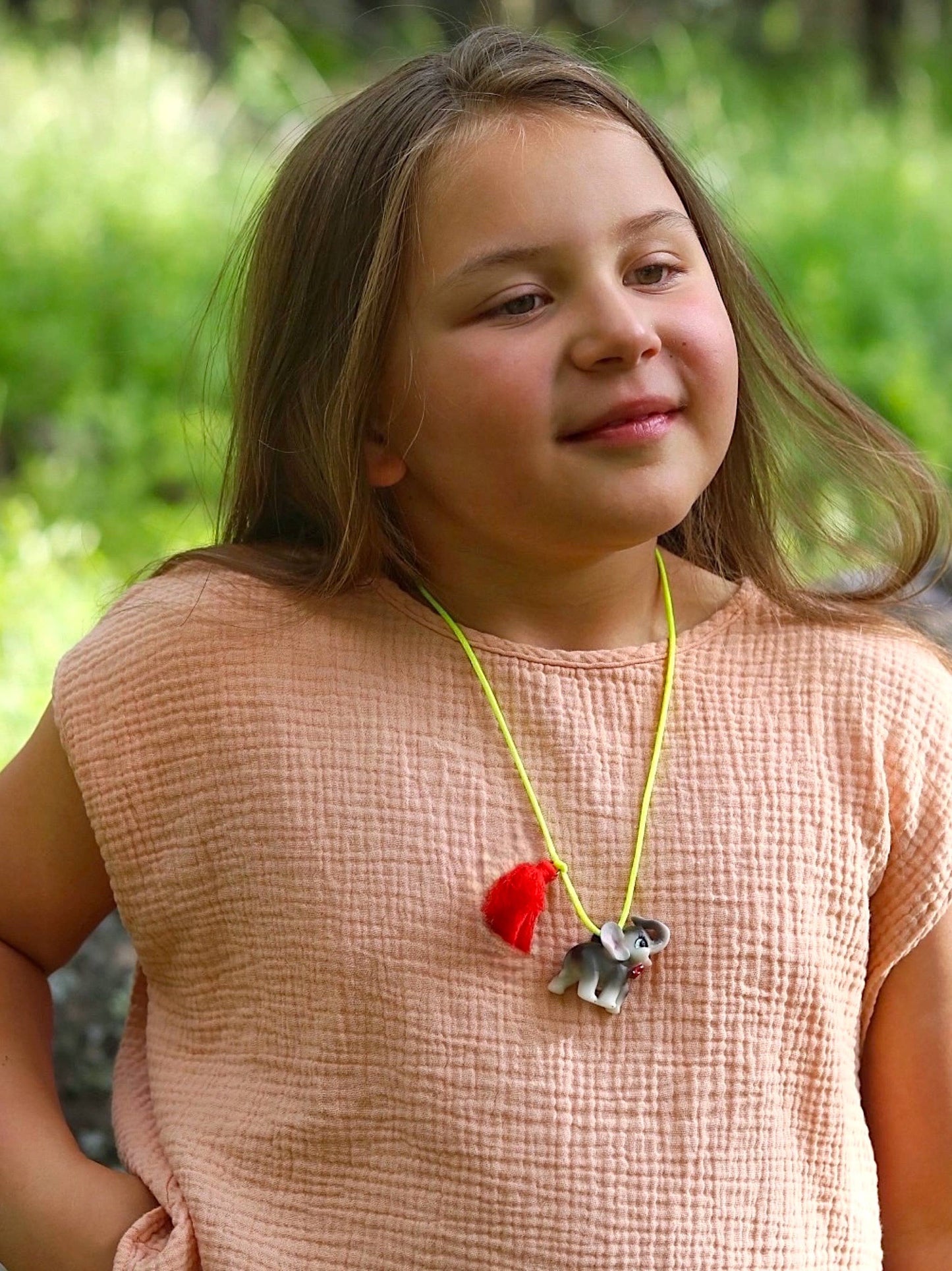 Young child wearing a necklace with an elephant pendant in a natural setting