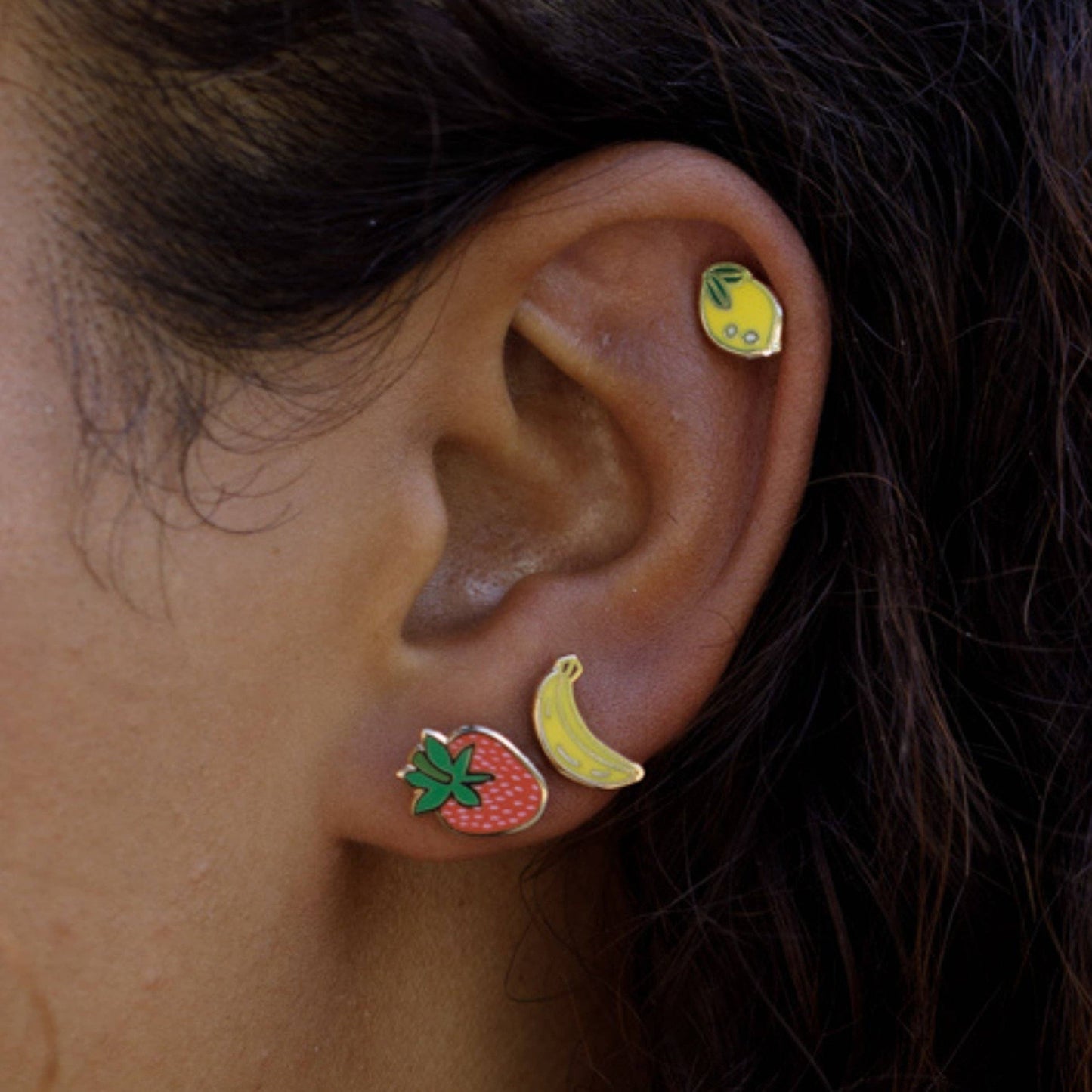 Close-up of an ear wearing fruit-themed earrings.