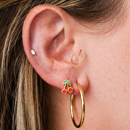Close-up of an ear with gold hoop earrings and a cherry-themed earring.
