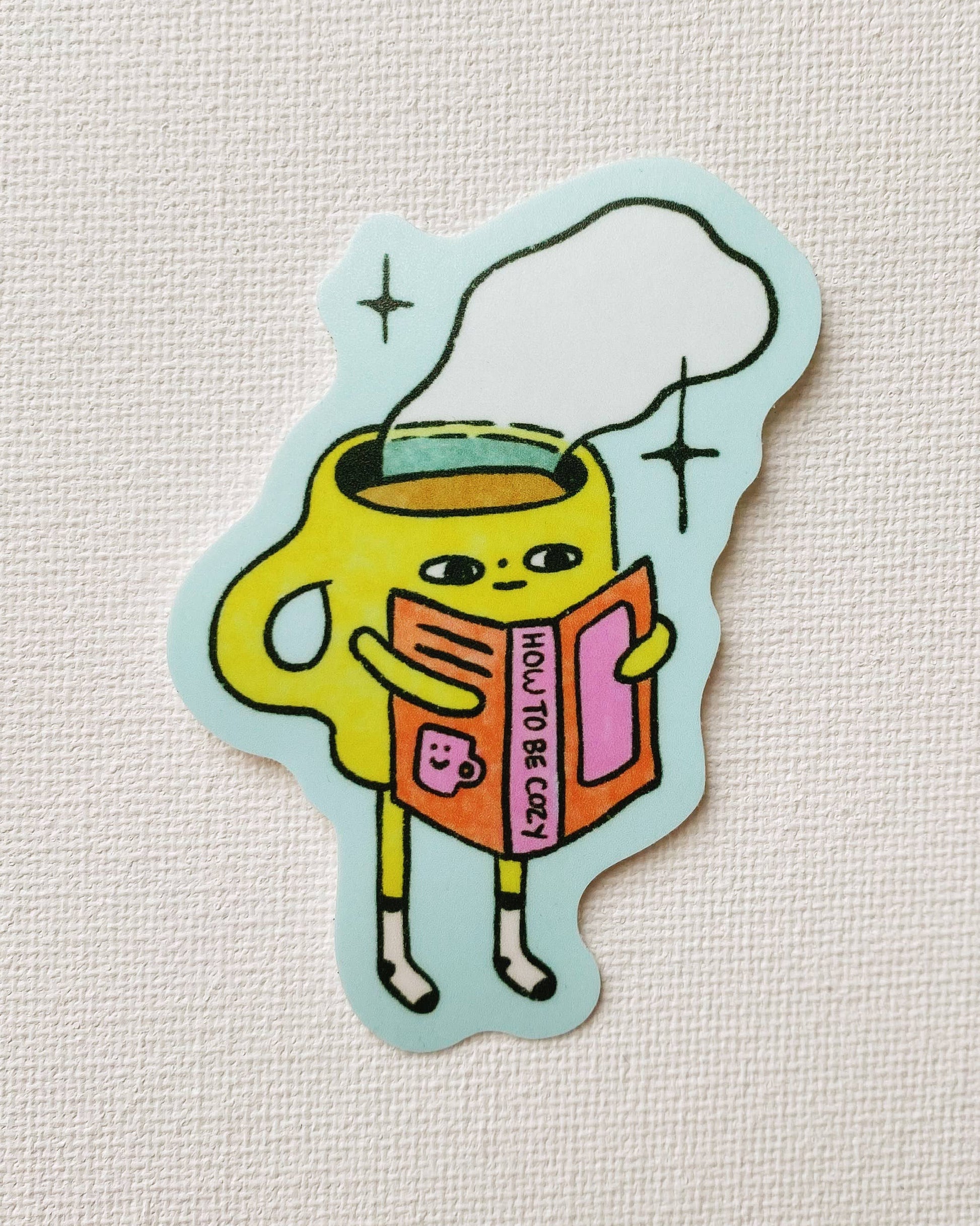 Sticker of a yellow cup character holding a book on a light gray background