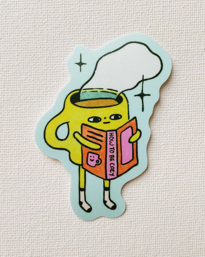 Sticker of a yellow cup character holding a book on a light gray background