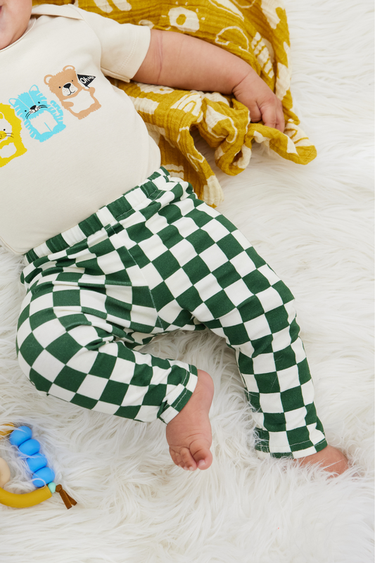 chubby 7 months old baby lying on a white furry rug wearing a onesie and green and white checker leggings.