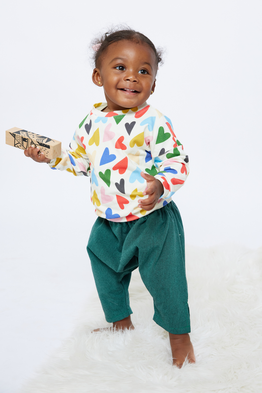 smiling baby holding a block and wearing gender free, colorful baby clothes