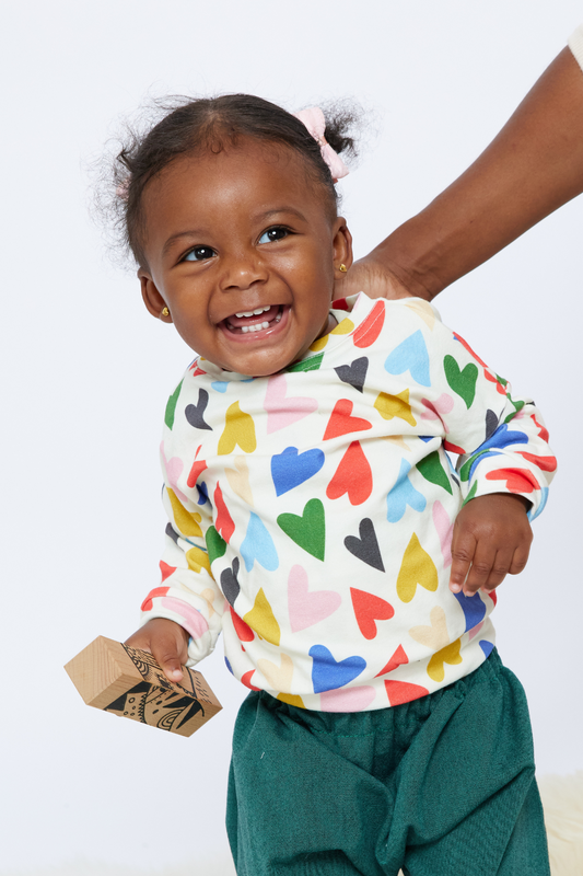 smiling baby holding a block and wearing a colorful organic cotton top with hearts