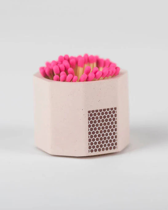 Pink matches in a hexagonal container with a honeycomb pattern on a light gray background