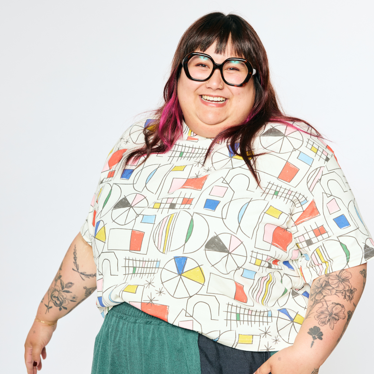 Person wearing a colorful geometric-patterned shirt with tattoos visible on arms.