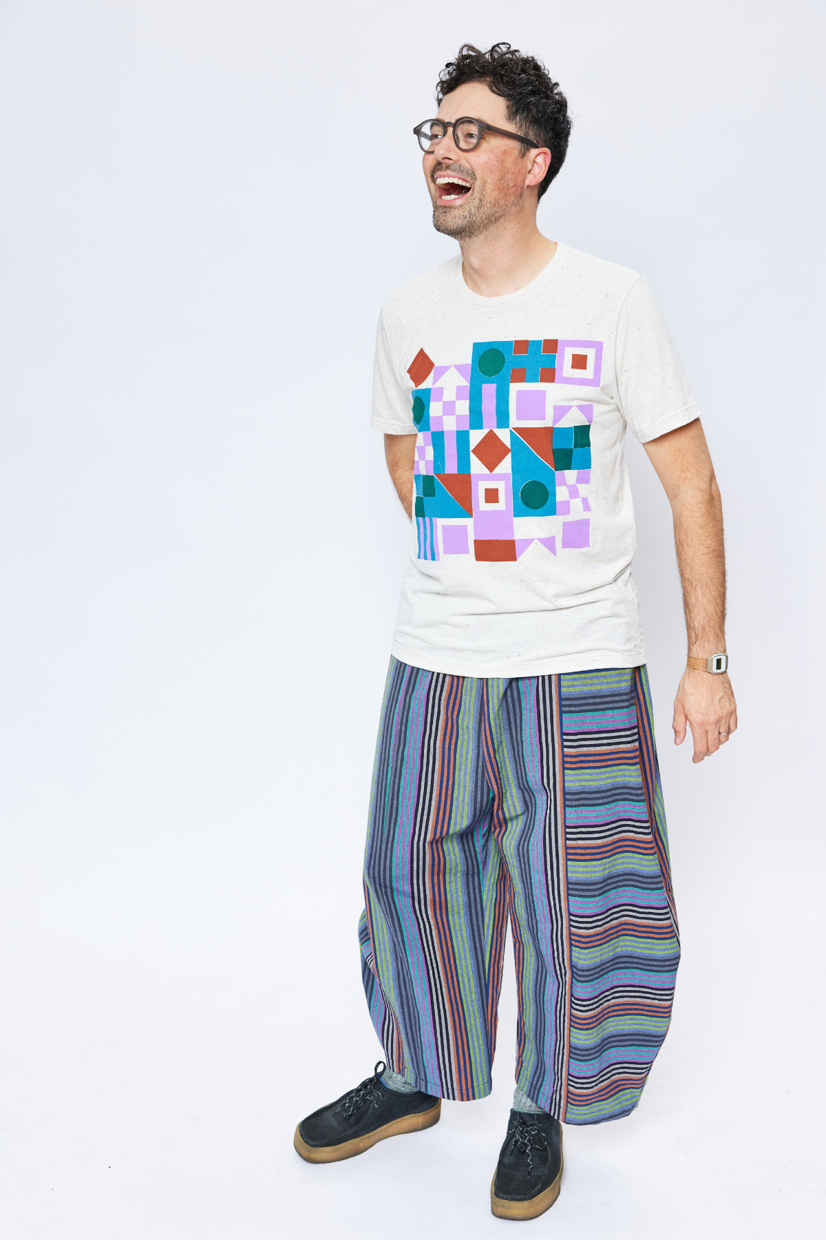 tall man wearing colorful striped barrel leg pants and a graphic tee. he's laughing.