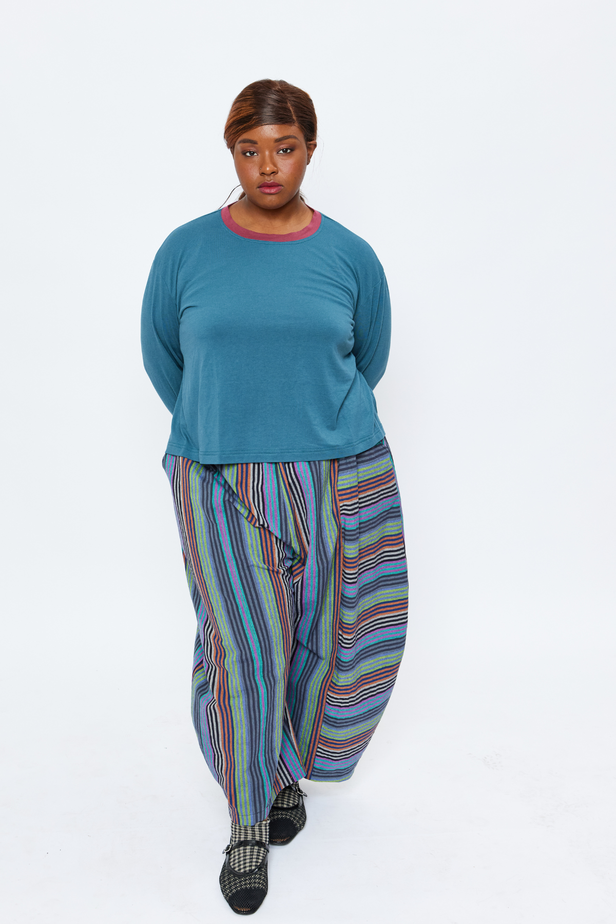plus size woman standing and wearing sustainable slow fashion garments including a blue bamboo top and colorful striped barrel leg pants