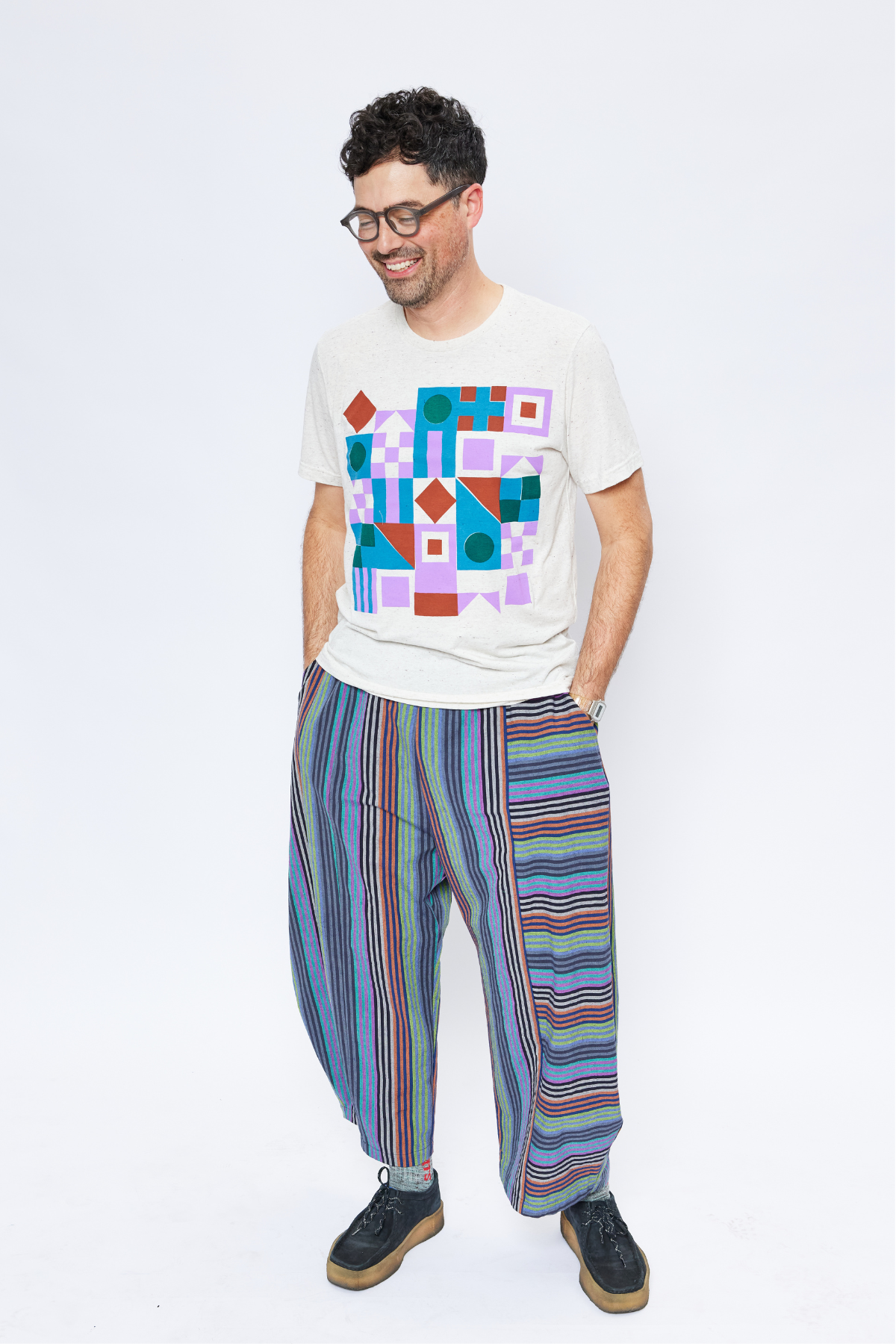 tall man wearing glasses with his hands in his pockets. He's wearing sustainable stripe cotton pants and a hand-designed t-shirt.