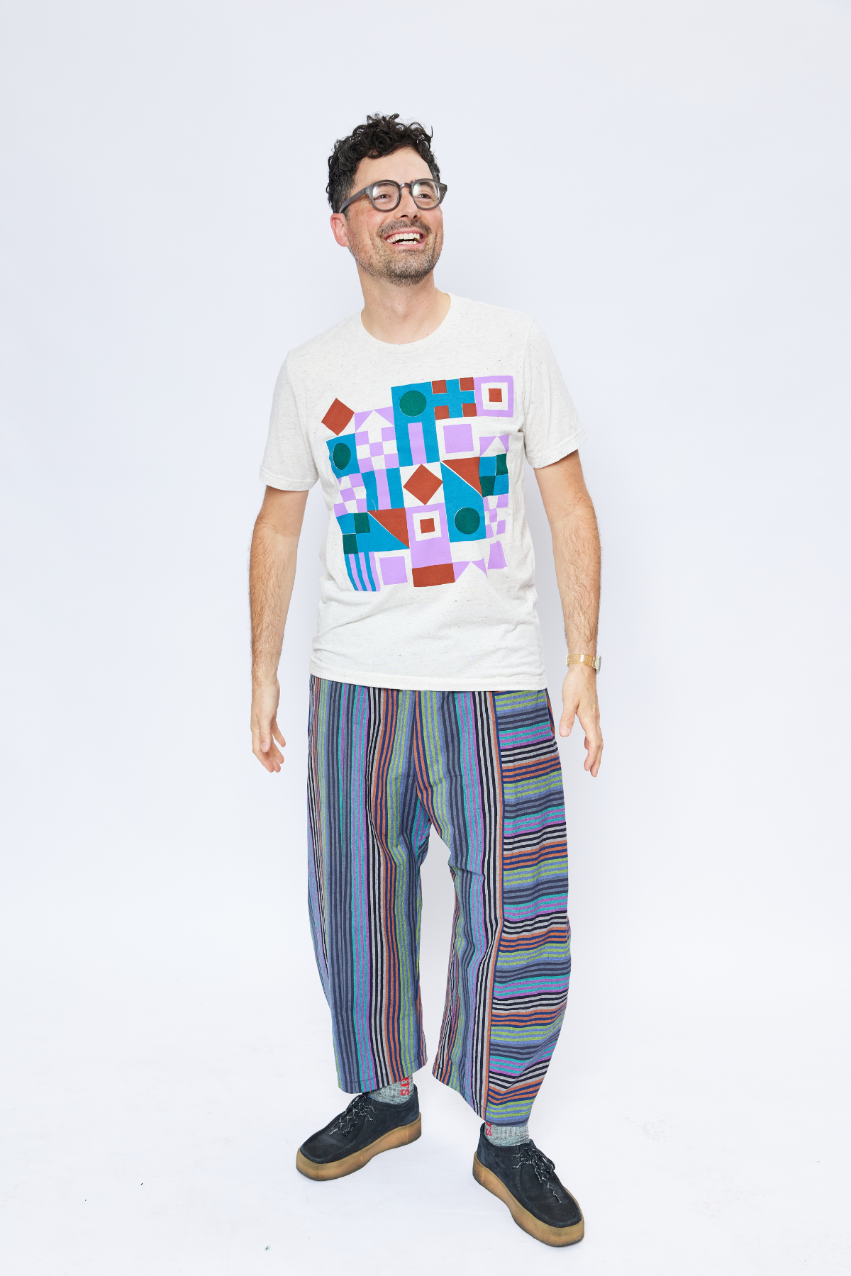 Tall man wearing glasses and smiling. He's wearing a hand-printed t-shirt by Earth Cadets and sustainable cotton stripe pants with pockets.