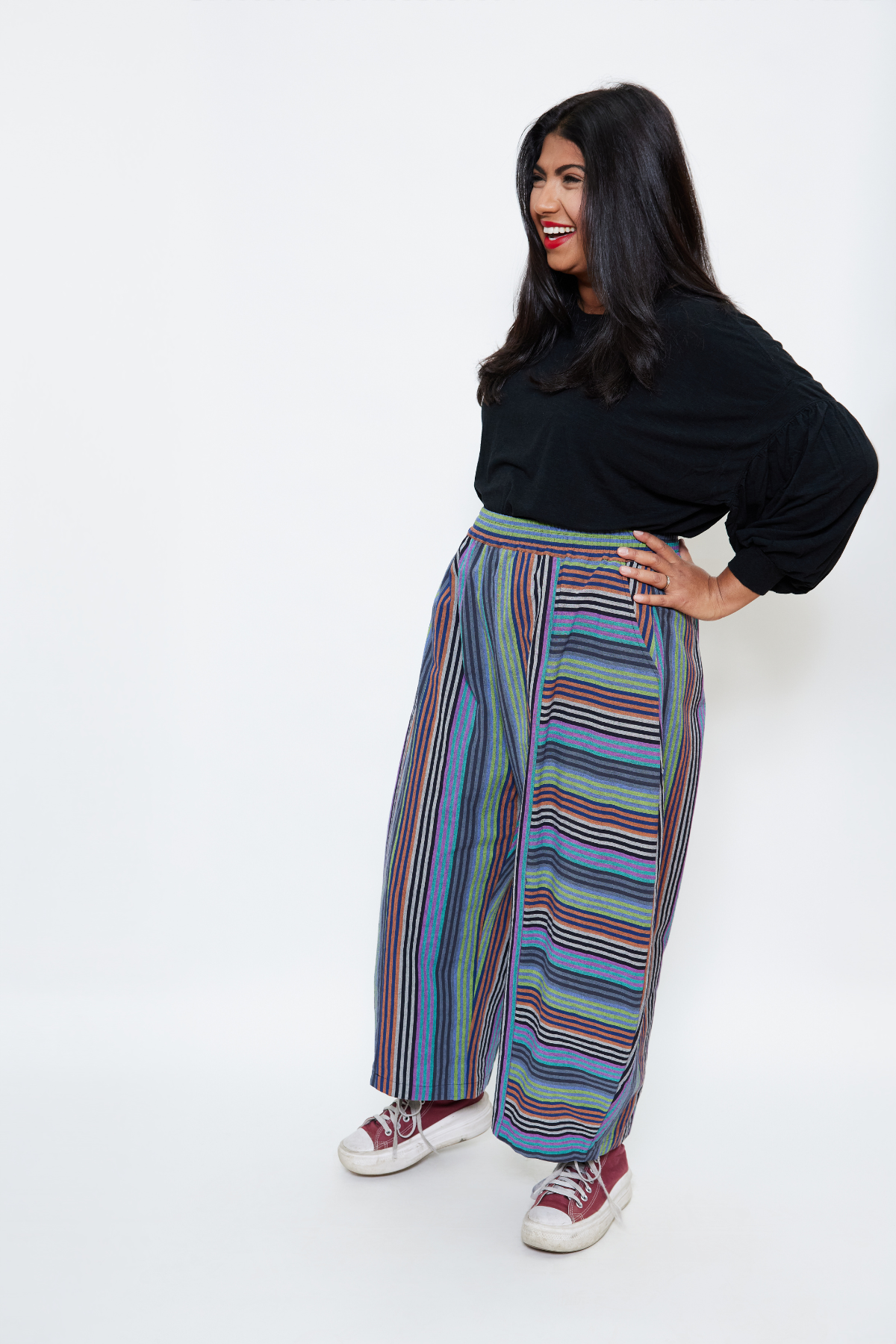 midsize woman standing with her hands on her hips. she's wearing a black top tucked into slow fashion colorful striped pants.