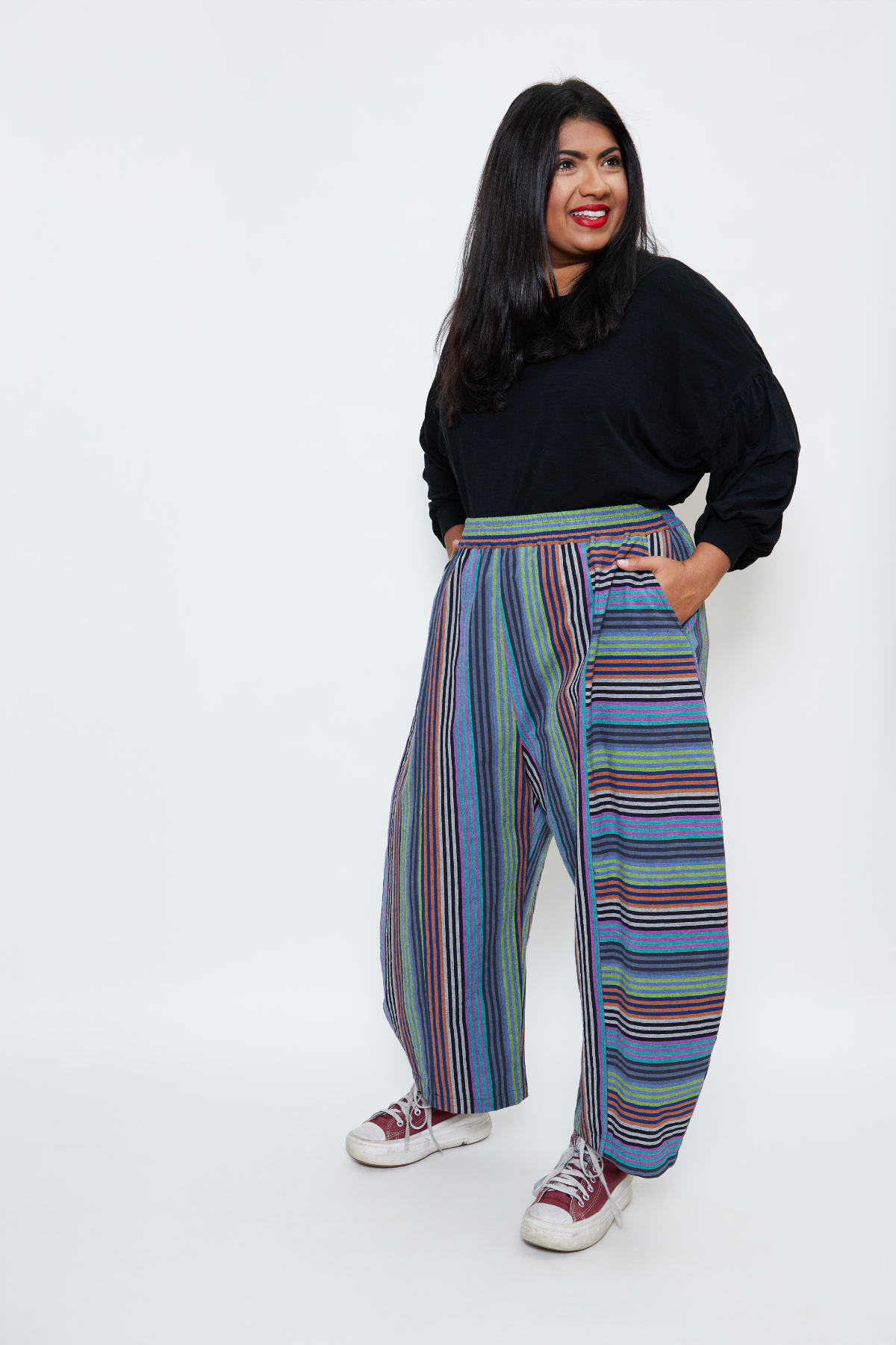 Cool mom standing with her hands in her pockets. She's wearing sustainable cotton pants with colorful stripes.